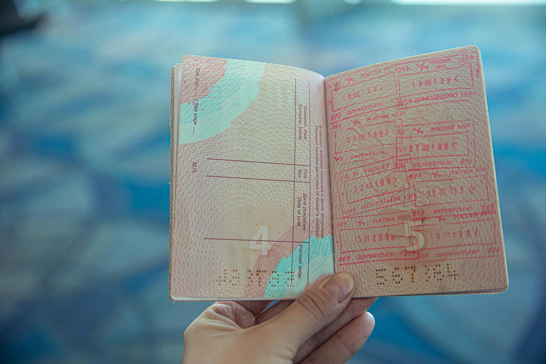 Close-up view of an open passport displaying various travel stamps in an airport setting. on Points and Pathways