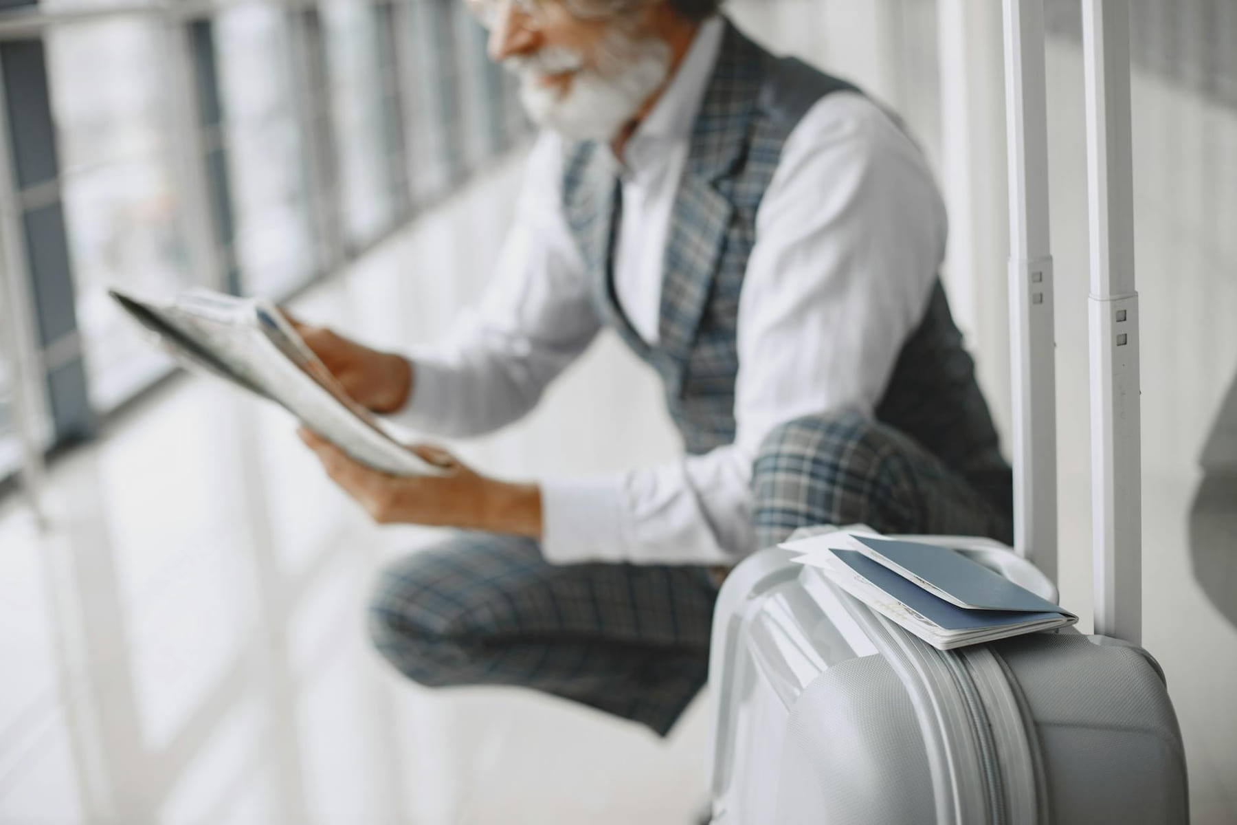 Adult man in plaid suit reads newspaper with suitcase at airport terminal. on Points and Pathways