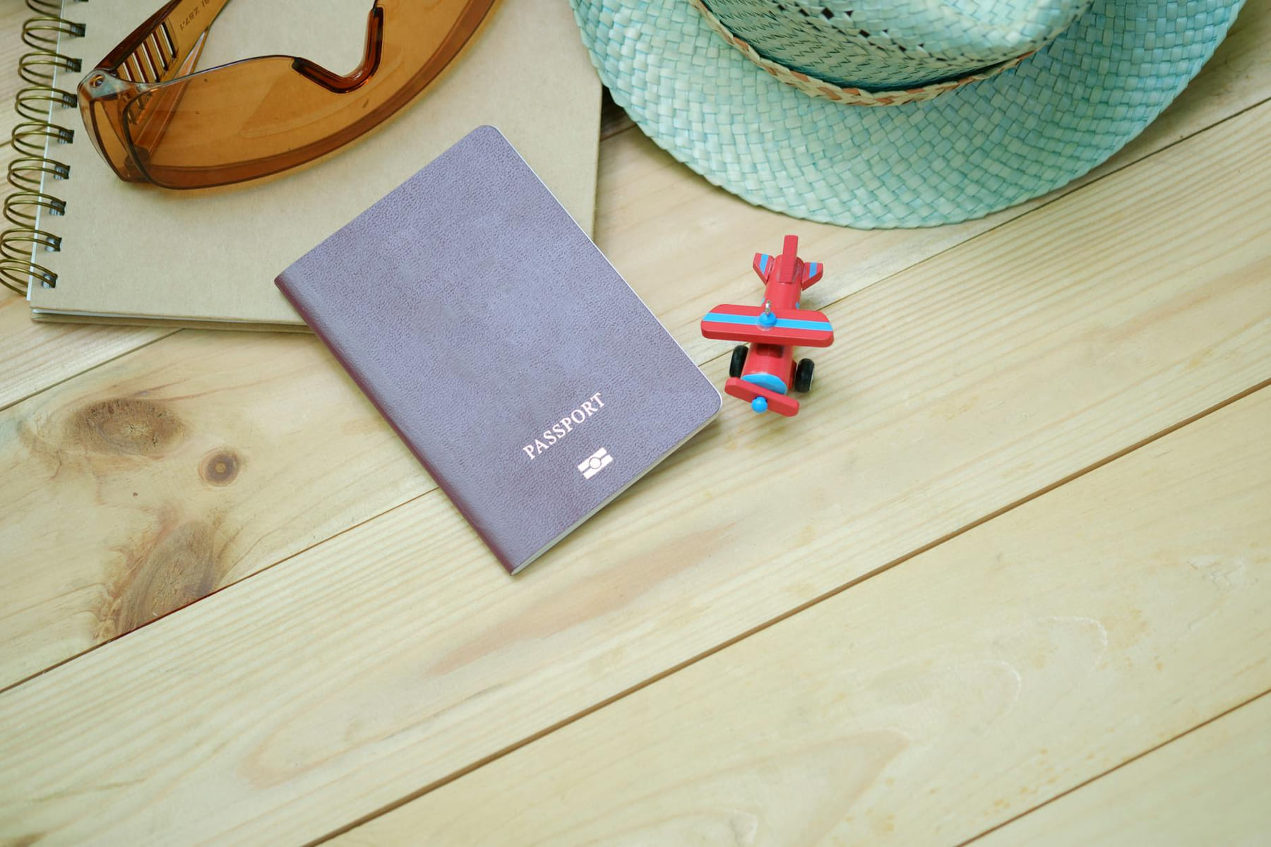 Flat lay of travel essentials including passport, notebook, toy airplane, sunglasses, and straw hat. on Points and Pathways