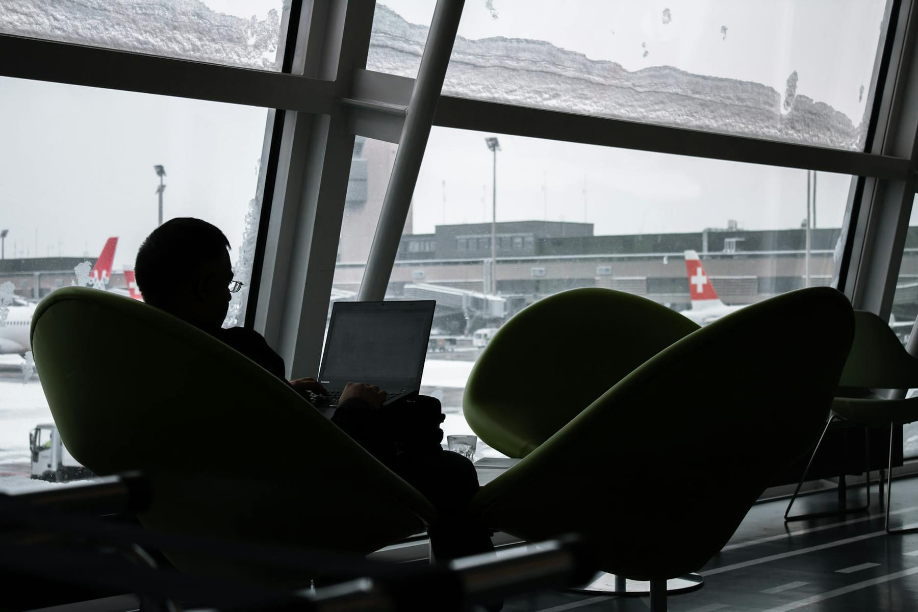 Silhouette of a man working on laptop at airport lounge with planes outside. on Points and Pathways