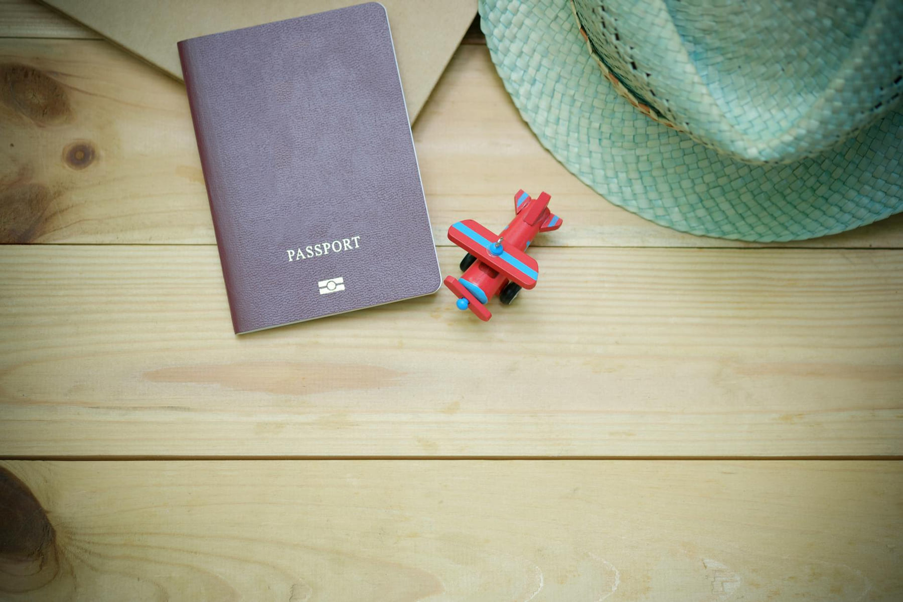 Flat lay of a passport, straw hat, and toy airplane on a wooden surface. on Points and Pathways