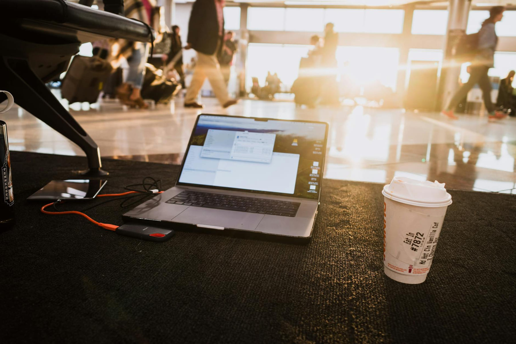 Laptop and coffee cup on airport floor with passengers walking by in warm sunlight. on Points and Pathways