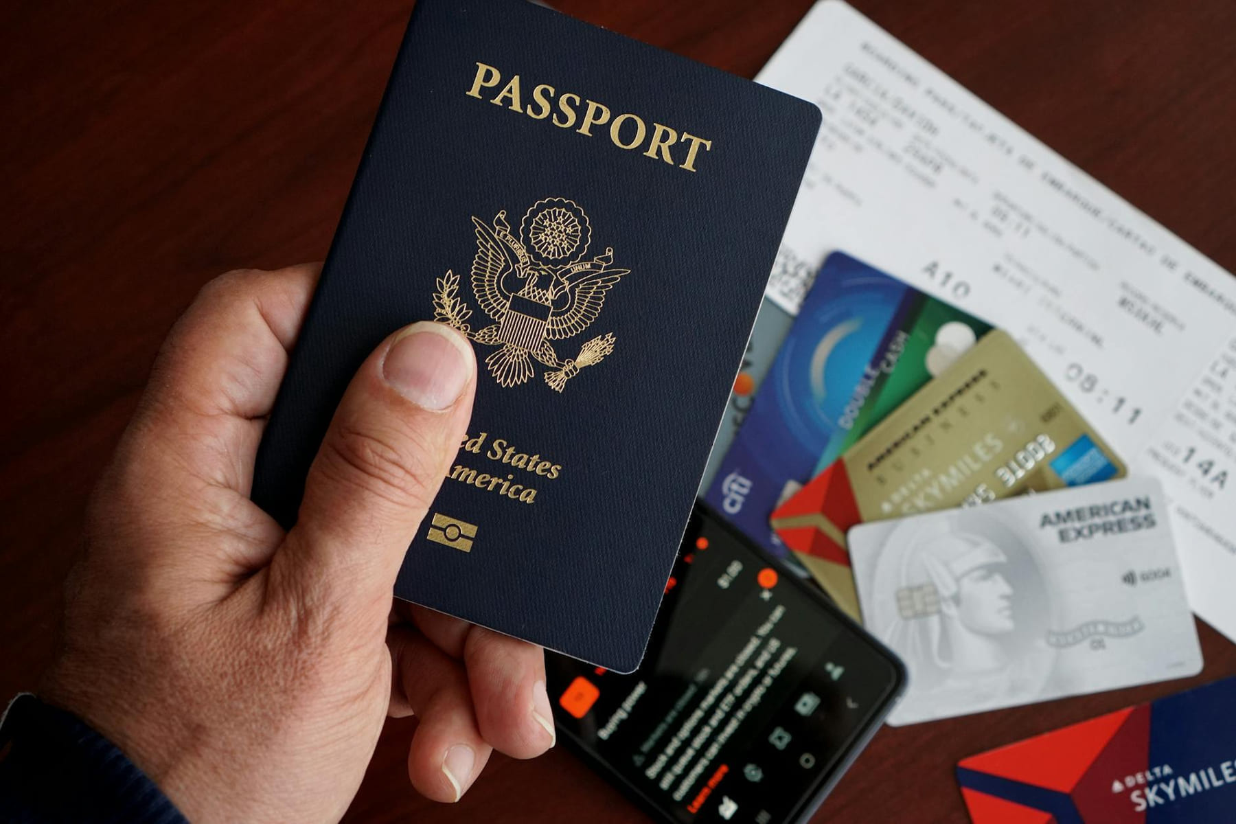 A close-up of a US passport with credit cards, tickets, and a mobile phone on a table. on Points and Pathways