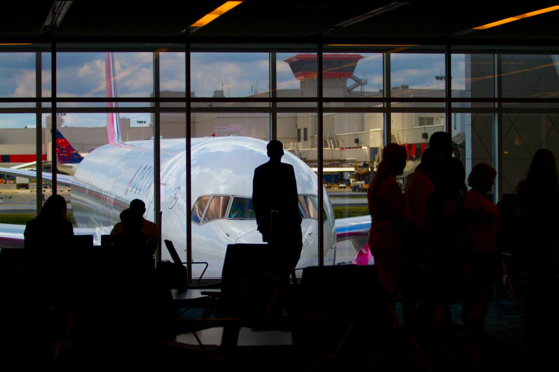 Silhouettes of travelers waiting at an airport terminal with an airplane visible through the window. on Points and Pathways